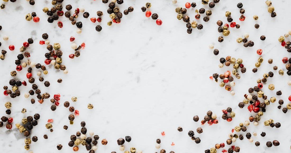Mixed whole peppercorns scattered on a marble countertop showing the variety of fresh spices used in electric pepper grinders