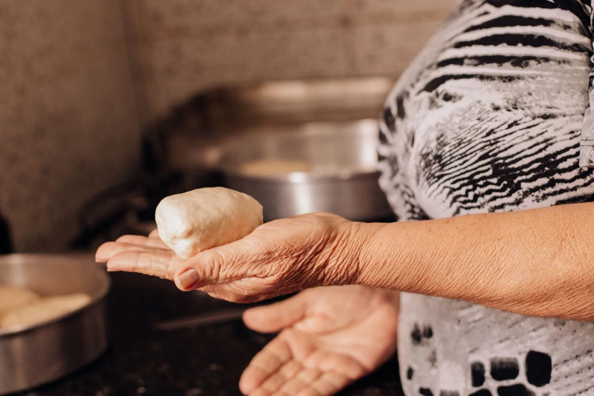 Close-up of an older person's hands gently holding a piece of dough in a warm, home kitchen setting.