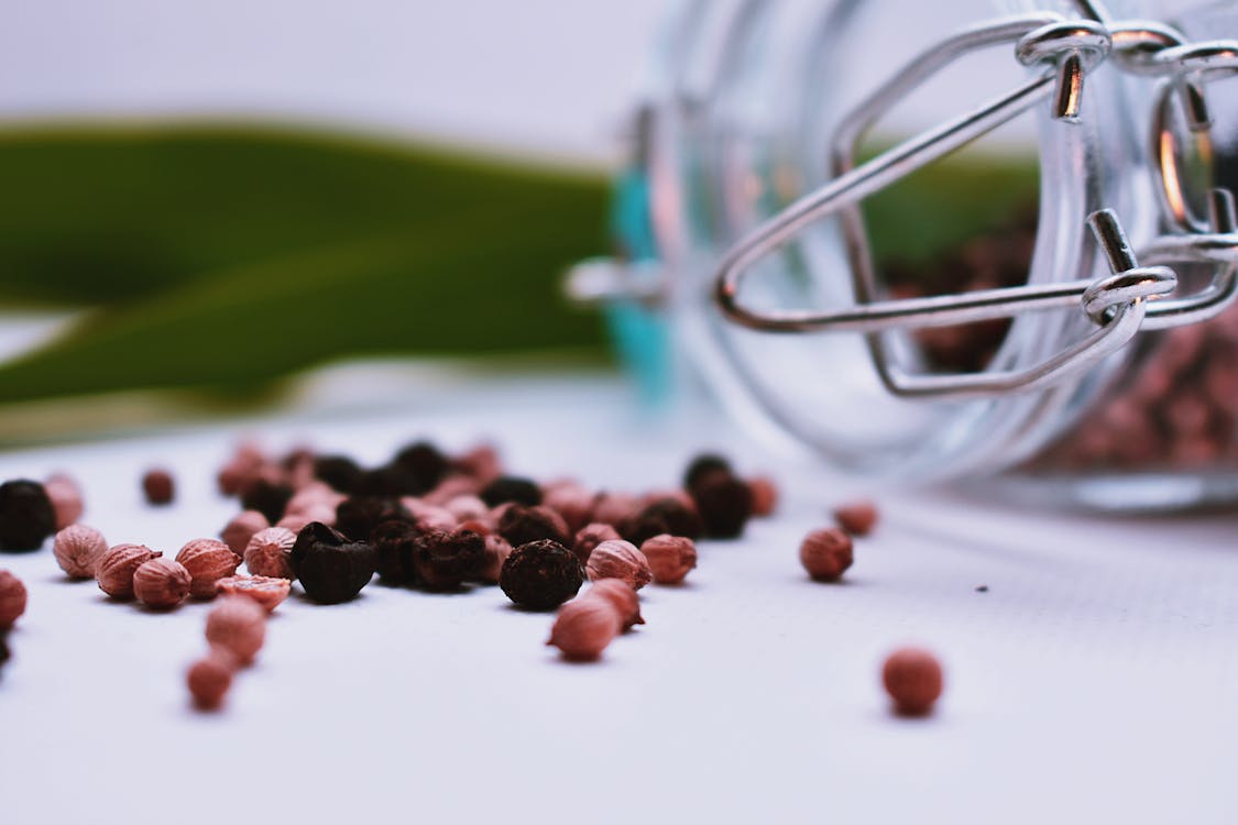 Whole black and pink peppercorns spilling from a glass jar, ready for fresh grinding
