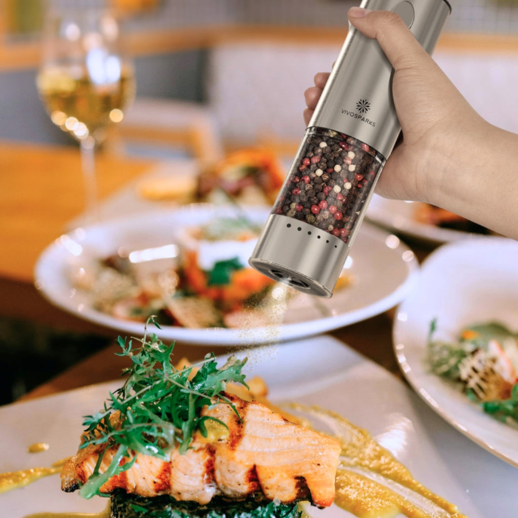 Hand holding a pepper grinder over a plate of food with a blurred background