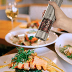Hand holding a pepper grinder over a plate of food with a blurred background